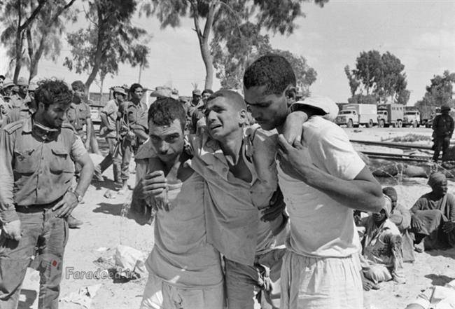 دو اسیر مصری در مقابل سربازان اسرائیلی یک اسیر مجروح را حرکت می‌دهند.