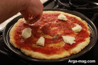 قرار دادن پنیر پیتزا روی خمیر پیتزا 